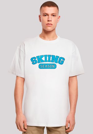 White T-shirt with short sleeves, featuring blue text "SKIING" above "SEASON" in a bold font. Soft cotton material, relaxed fit.