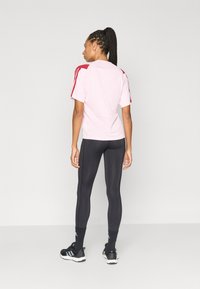 Lichtroze sportshirt met rode accenten, gecombineerd met zwarte legging. Het shirt heeft korte mouwen en een comfortabele, losse pasvorm.