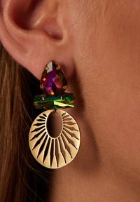Gouden oorbellen met een multifacet paarse edelsteen, een groene accentsteen en een uitsnede cirkelvormig ontwerp met driehoekige stralen.
