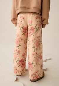 Virágmintás bőszárú nadrág lágy rózsaszín anyagból, részletes rózsa- és levélmintával. Két hátsó zsebbel és kényelmes szabással.