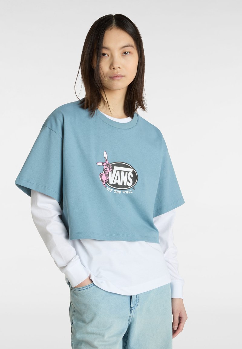 Lyseblå cropped bomulds-t-shirt med et pink kaninmotiv og sort "VANS" logo, lagd ovenpå en hvid langærmet skjorte.