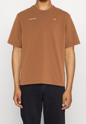 T-shirt en coton marron avec un col rond, des manches courtes et des logos blancs imprimés sur la poitrine ; coupe décontractée avec un ourlet droit.