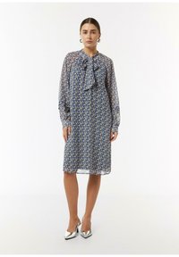 Blumenmusterkleid aus transparenter blauer Stoff mit langen Ärmeln, Schleifen-Halsausschnitt und knielanger Schnitt, kombiniert mit silbernen High-Heels.