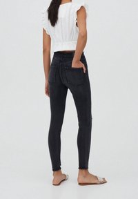 Mustat kapeat farkut, joissa on korkea vyötärö, takataskut ja rispaantuneet lahkeet. Yhdistetty valkoiseen kirjailtuun toppiin ja koristeltuihin sandaaleihin.