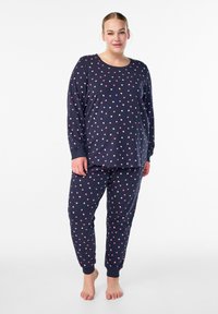 Navy blauwe pyjama set met een lange mouwen top en broek, met een patroon van kleine roze, witte en paarse harten; zacht, nauwsluitend en met ribboorden.