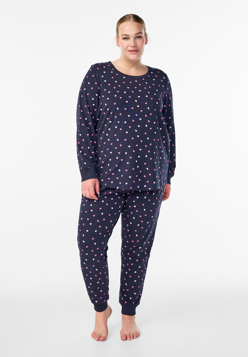 Navy blauwe pyjama set met een lange mouwen top en broek, met een patroon van kleine roze, witte en paarse harten; zacht, nauwsluitend en met ribboorden.