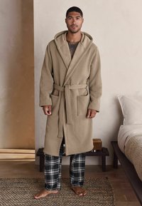 Beež kapuutsiga rüü tekstureeritud voodriga, isesiduv vöö ja kaks esikülje taskut. Kombineeritud mustvalgete ruuduliste magamispükstega. Kergelt jalasolekuta.