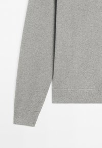 Close-up of a long-sleeve gray knit sweater showing the sleeve and bottom hem with ribbed cuffs and waistband.