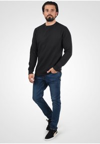 Must värvitud pikkade varrukatega sweatshirth, millel on eriline tekstuur ja soonikdisain. Kandmise hõlbustamiseks on selga tõmmatud sinised teksad ja mustad sportlikud jalanõud. Kanna mugavalt ja stiilselt.