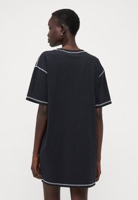 Juoda per didelė t-shirt su trumpomis rankovėmis, kontrastingais siūlais kraštuose ir laisvu siluetu. Lygi medvilnės audinys.