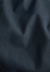 Tejido oscuro con una textura suave, que presenta arrugas sutiles y un patrón uniforme. El material parece duradero y ligero.