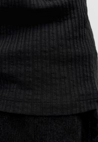 Close-up van zwart geribbeld gebreide stof over zwart denim stof.