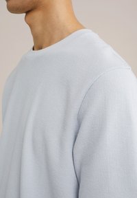 Ljust blå strukturerad stickad sweatshirt med rund halsringning och korta ärmar, med ett subtilt ribbat mönster på tyget.