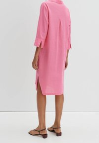 Rosa linneklänning med krage, trekvartslånga ärmar, sidofickor och bakfåll. Bärs med svarta sandaler med remmar.