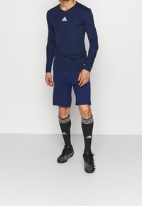 Pitkähihainen tummansininen urheilupaita, tummansiniset shortsit, mustat jalkapallosukat, joissa on valkoiset raidat, ja mustat nappulakengät, joissa on tekstuuri.