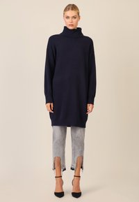 Granatowy sweter z golfem, luźny i z długimi rękawami, zestawiony z szarymi dżinsami 3/4 z frędzlami na końcu i akcentami.