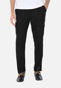 Pantaloni cargo neri con tasche laterali, una vita con cordino elastico e vestibilità rilassata. Indossati con scarpe nere e dettagli gialli.