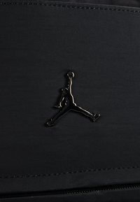 Schwarzer Stoff mit einem glänzenden schwarzen "Jumpman"-Logo. Die Oberfläche ist mit feinen Rillen strukturiert, die die Silhouette des Logos hervorheben.