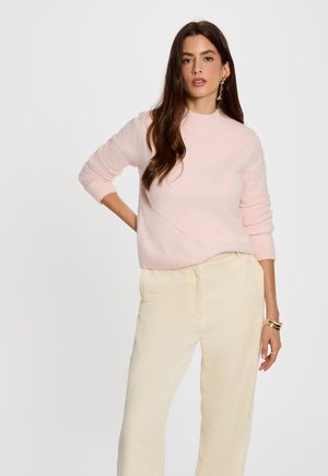 Soft pink sweater with a high neck, long sleeves, and textured fabric, paired with light beige corduroy pants. Simple design, no patterns.