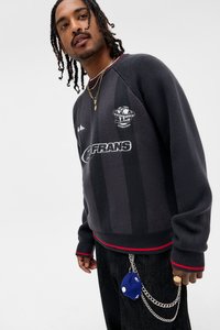 Mörkgrå texturerad tröja med röda detaljer, med logo och ränder, kombinerad med mörka jeans och ett kedje-nyckelband.