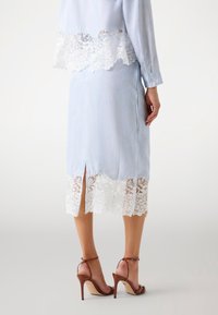 Fustă albastră deschis cu dantelă albă la tiv și o slit la spate, asortată cu sandale cu toc înalt și curele maro. Textură netedă.