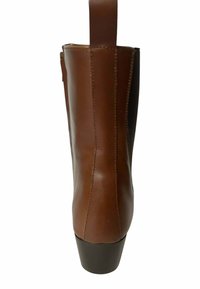 Bota de tobillo de cuero marrón con textura lisa, punta redondeada y tacón bloque negro. Cuenta con una cremallera lateral y una lengüeta en la parte superior.