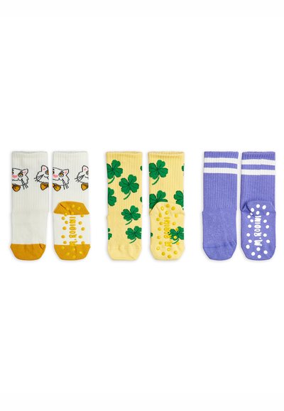 Three pairs of children's grip socks: white with cat faces and orange toes, yellow with green four-leaf clovers, and purple with white stripes and grip dots.