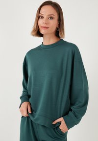 Felpa verde acqua realizzata in tessuto morbido, con scollatura a girocollo, spalle scese e maniche lunghe con polsini a coste. Design semplice.