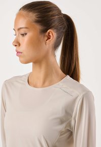 Licht beige atletisch shirt met lange mouwen, gemaakt van een textuurstof, ronde halslijn en contrasterende stiksels. Logo "SWEDEMOUNT" op de schouder.