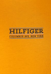 T-shirt di cotone gialla con testo stampato blu e bianco: "HILFIGER COLUMBUS AVE. NEW YORK," dal tessuto liscio e dal design casual.