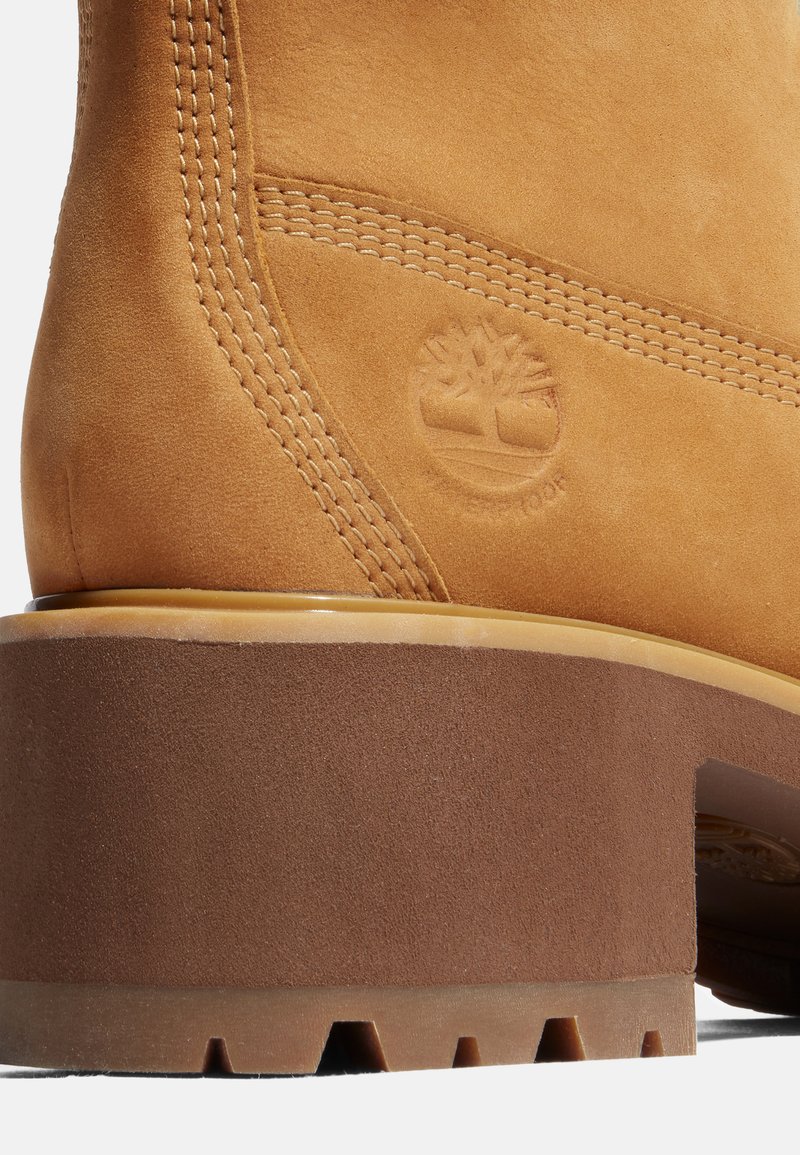 Botte en suède beige avec une semelle en caoutchouc marron. Comprend des détails cousus et un logo d'arbre surélevé sur le côté. Bout arrondi avec des accents texturés.