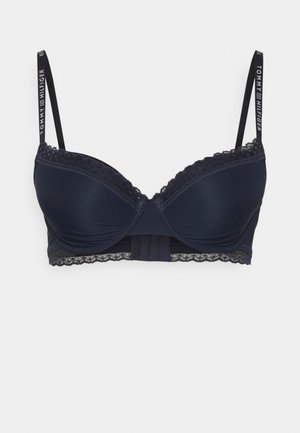 Tumedat sinine polsterdatud rinnahoidja siledast kangast, pitsääristega, reguleeritavad rihmad ja konks- ja silmadega tagasulgemine. Tommy Hilfiger brändimine rihmadel.