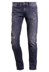 Jeans de mezclilla azul oscuro con corte slim, que presentan zonas desgastadas y sutiles arrugas. Diseño estándar de cinco bolsillos con herrajes metálicos.