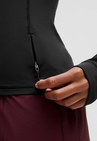 Pikendustega must sportlik särk, millel on kennitasku, koos marooni värvi sportlike pükstega. Kanga pind tundub sile ja veniv.