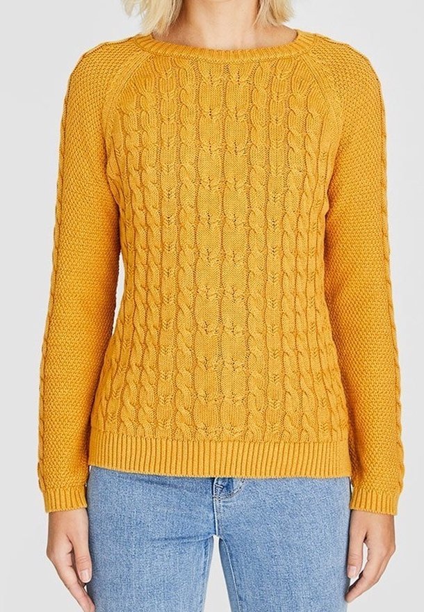 Pull en maille jaune moutarde avec motifs torsadés et texturés, col rond, et ourlets côtelés aux poignets et à l'ourlet. Porté avec un jean bleu.