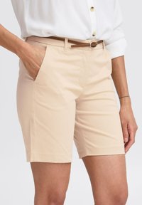 Beige pamut rövidnadrág egyenes szabással, oldalsó zsebekkel és barna övvel. Az anyag sima textúrájú és letisztult vonalvezetésű.