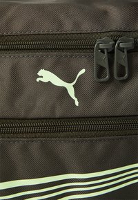 Svart stoffpose med dobbel glidelås; dekorert med en lys grønn Puma-logo og tynne gule og blå striper.