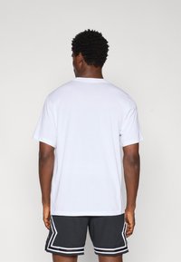 Hvid kortærmet bomulds-t-shirt med rund hals, set fra bagsiden, parret med sorte sportshorts med hvide detaljer.