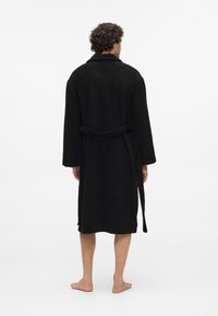 Svart, struktureret badekåbe med lange ærmer, sjalskrave og bindebånd, set fra ryggen. Gulvlængde med en afslappet pasform.
