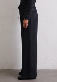 Zwarte, high-waisted broeken met een rechte snit, gemaakt van gladde stof. Beschikt over een elastische tailleband met een koord.