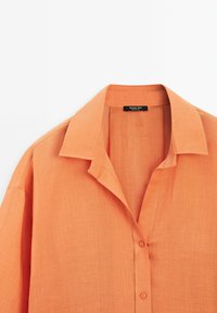 Oranje linnen overhemd met een kraag, voorste placket met knopen en een zachte textuur. Label zichtbaar in het kraaggebied.