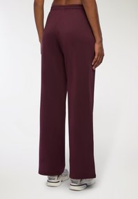 Pantaloni atletici bordeaux con vestibilità rilassata, cintura elastica e superficie liscia, abbinati a scarpe sportive grigie e bianche.