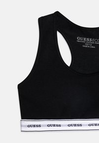 Soutien-gorge de sport en coton bio noir avec un design dos nageur. Caractérisé par une bande élastique blanche avec le logo "GUESS" et des rayures contrastantes en bas.