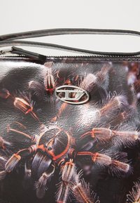 Black faux leather handbag featuring a detailed graphic design of spider-like features, accented with silver hardware. Zipper closure.