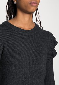 Maglione a coste grigio scuro con scollatura rotonda e dettagli arricciati sulle spalle. Presenta un motivo a maglia testurizzato.
