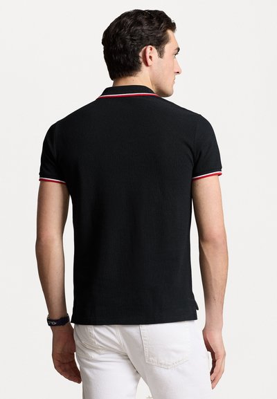 Black polo shirt with short sleeves, featuring red and white trim on the collar and sleeves. Fabric has a textured appearance.