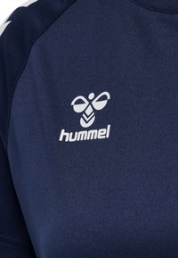Námořnické sportovní tričko vyrobené z látky s hladkou texturou, které má bílé logo Hummel a kontrastní bílé akcenty na ramenou.
