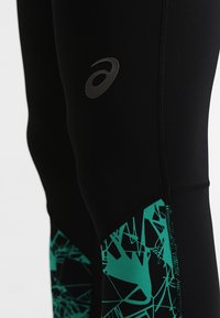 Leggings de sport noirs avec un motif géométrique abstrait en teal sur le bas de la jambe. Présente un petit logo argenté sur la cuisse. Texture lisse.