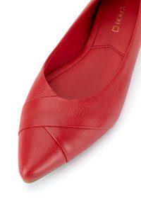 Červená kožená balerína s špičatou špičkou a křížovým designem na přední části. Hladký povrch a minimalistický styl. Žádné viditelné kovové prvky.