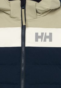 Veste matelassée avec capuche, design bicolore en beige, crème et marine, avec une fermeture éclair sur le devant et un logo sur la poitrine.